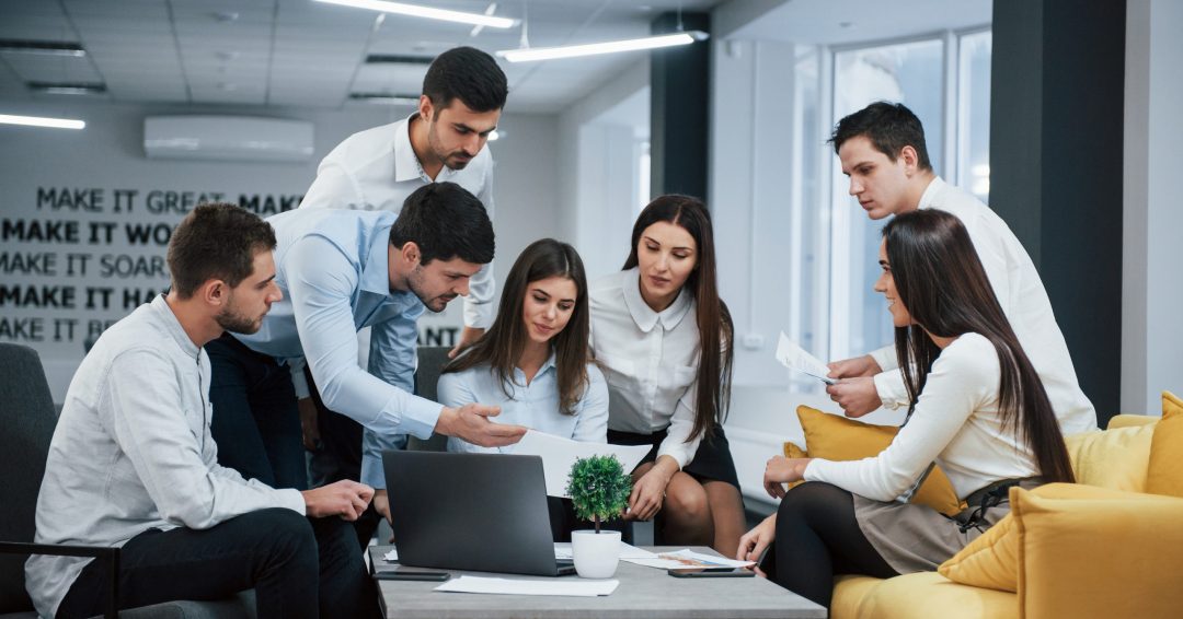 Guy shows document to a girl. Group of young freelancers in the office have conversation and working.